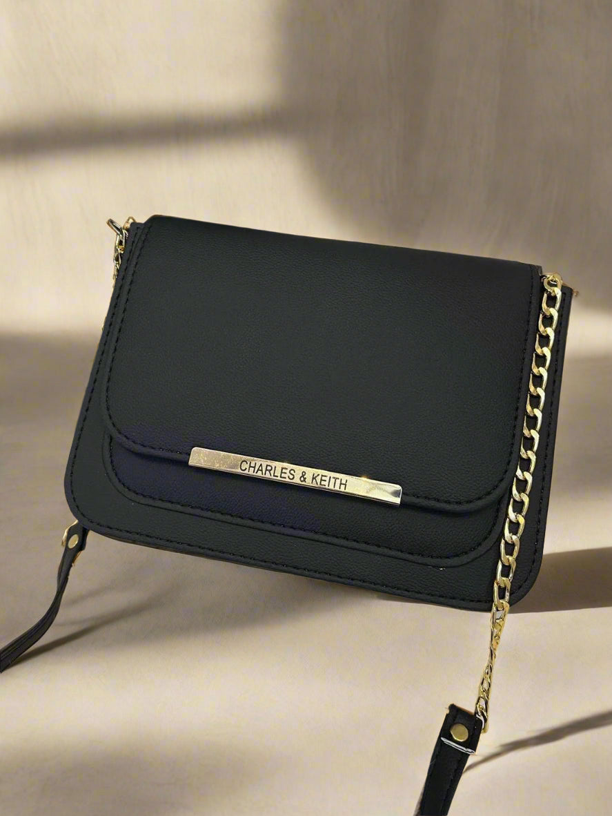 Black handbag with gold chain strap on a beige backgound