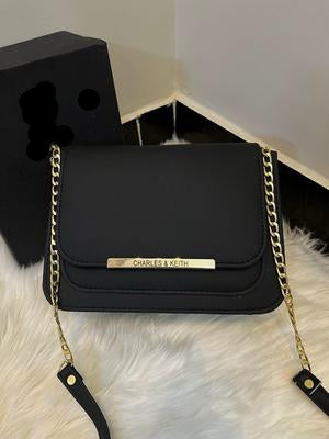 Black handbag with gold chain strap on a white surface.