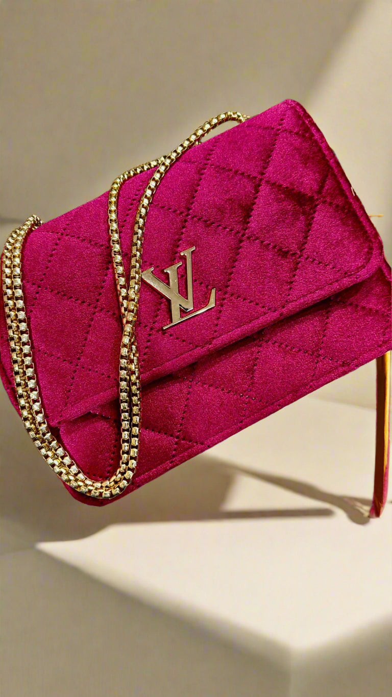 Red quilted handbag with gold chain and logo on a beige surface