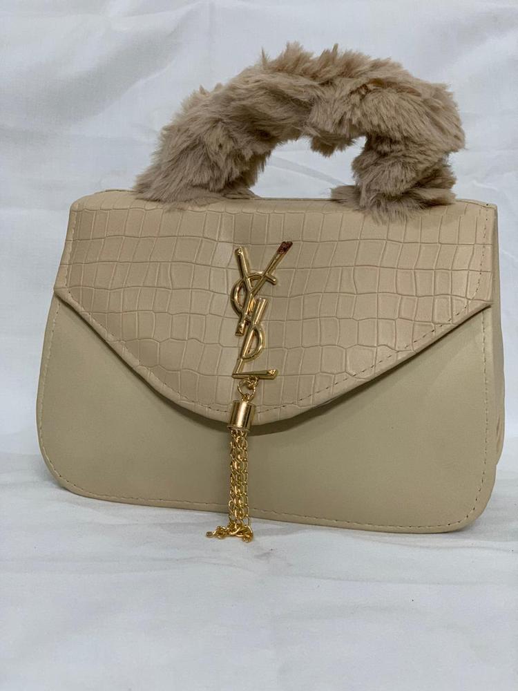 Beige handbag with fur handle and YSL logo on a white background