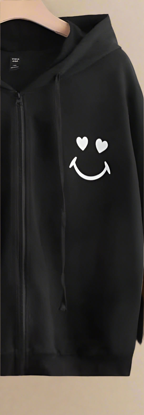Black hoodie with a smiley face design on a light beige background