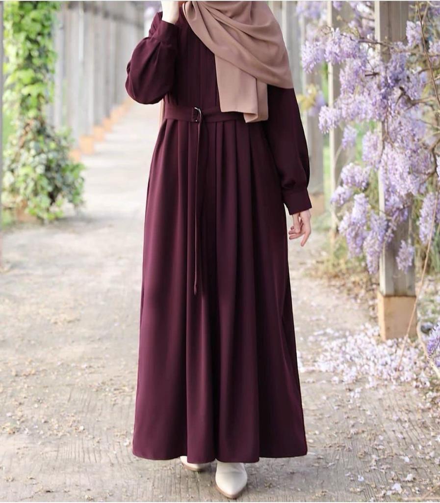 Person wearing a long burgundy dress with a beige hijab in a garden setting.
