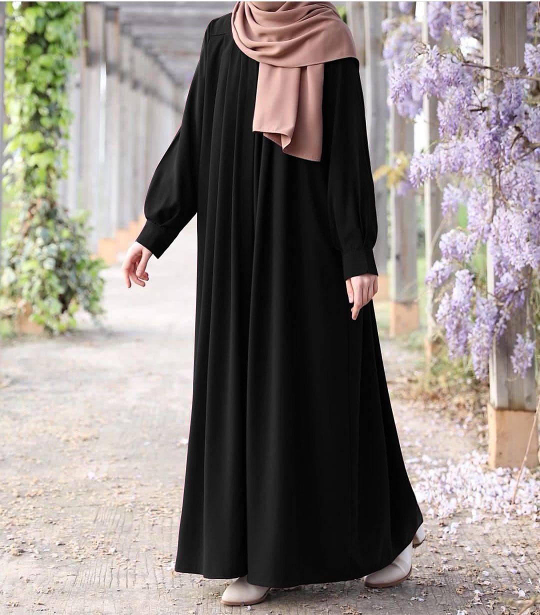 Person wearing a black abaya with a pink hijab in an outdoor setting with flowers.