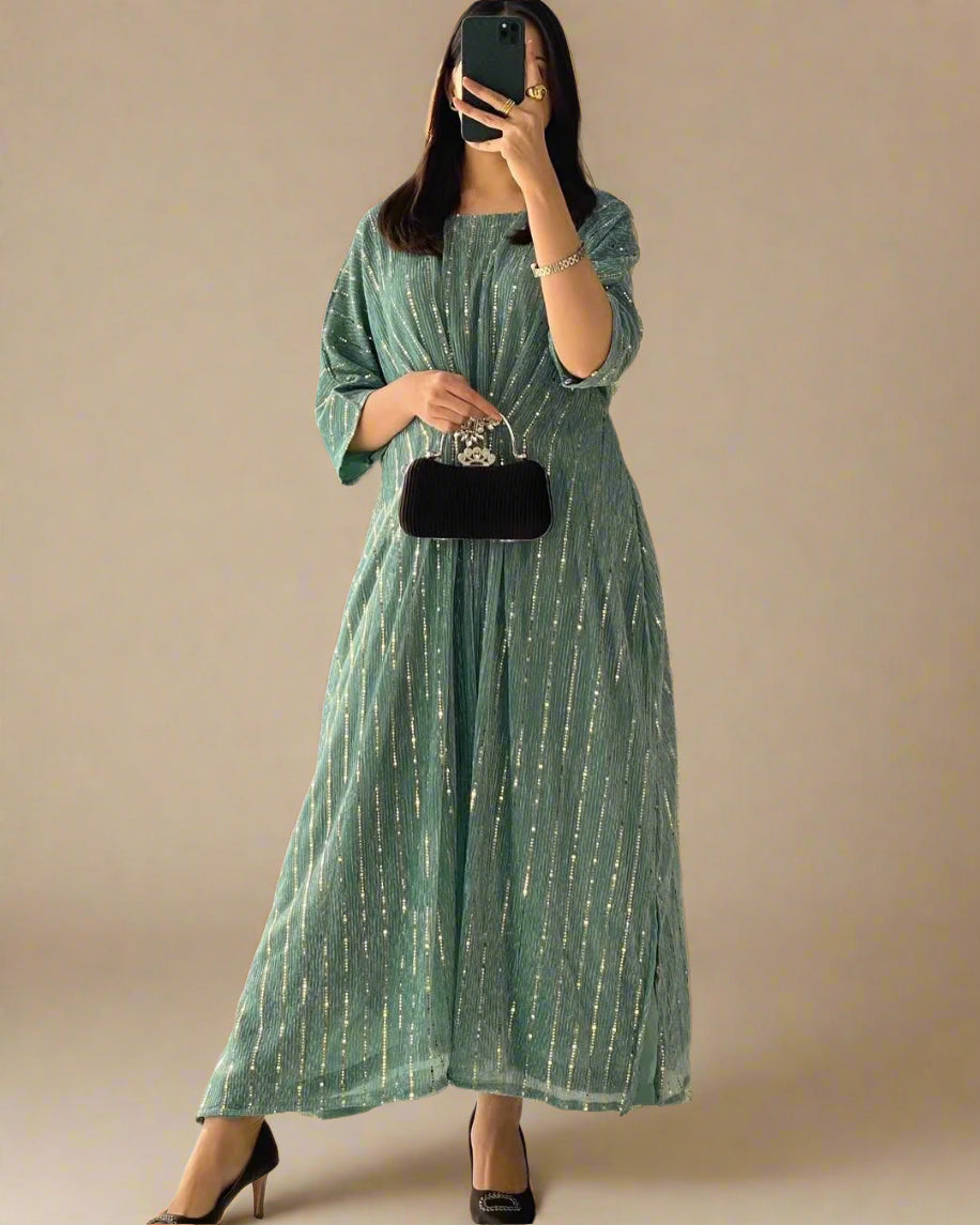 Woman wearing a green dress with gold stripes, holding a black handbag in a room.