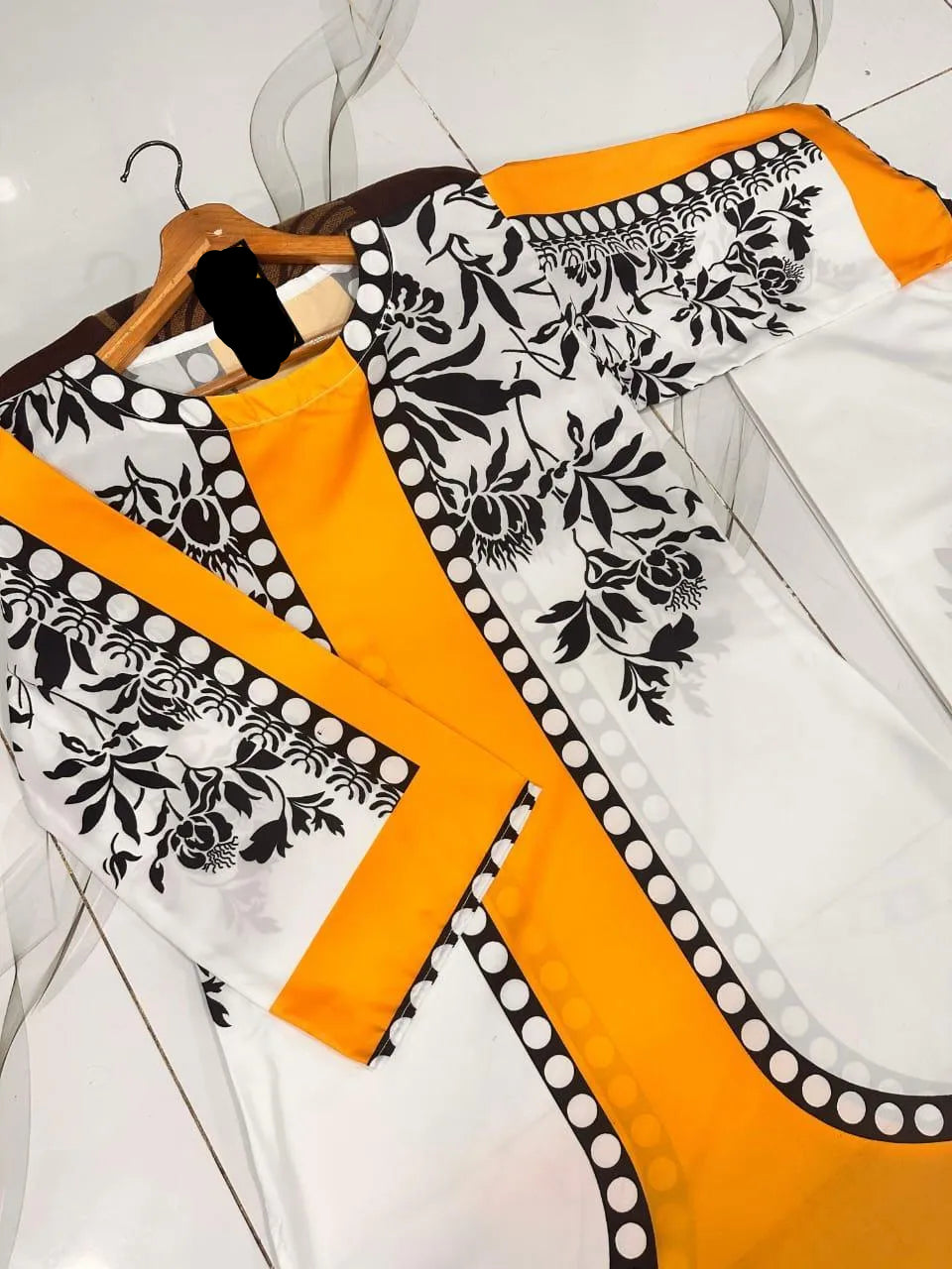 White shirt with black floral patterns and orange accents on a hanger.