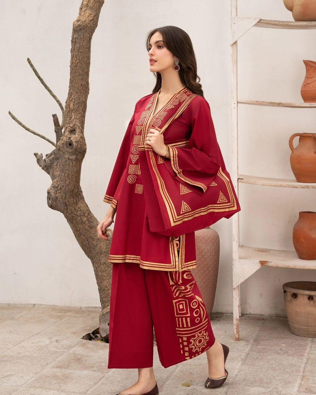 Woman wearing a red traditional outfit with gold patterns in an indoor setting.