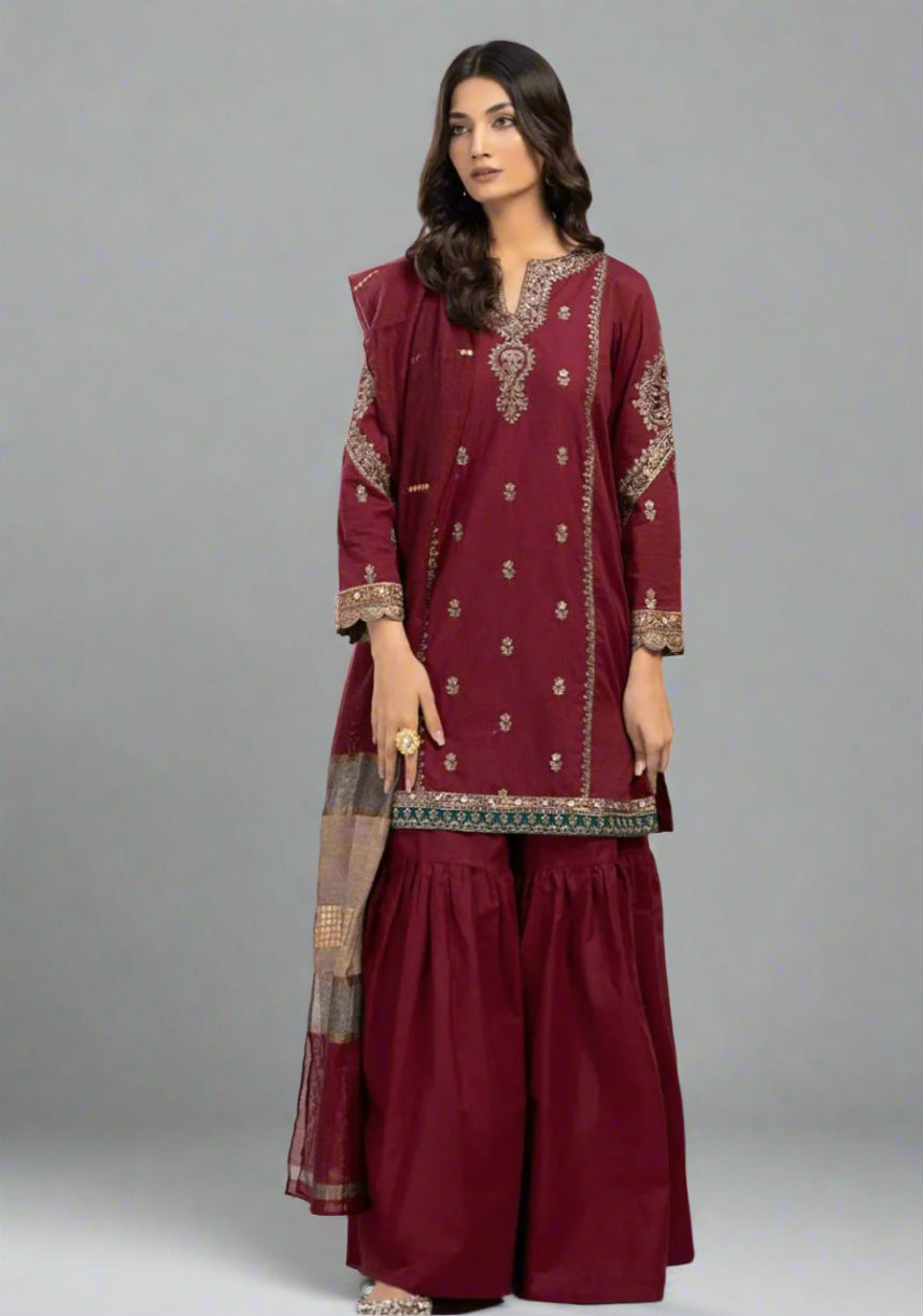 Woman wearing a maroon embroidered traditional outfit on a plain background