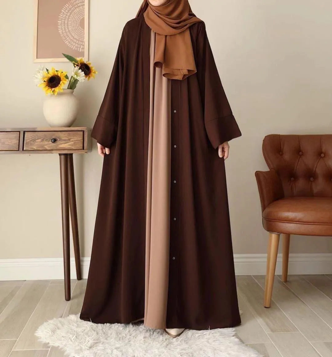 Person wearing a brown abaya with a matching hijab in a room with a table and chair.