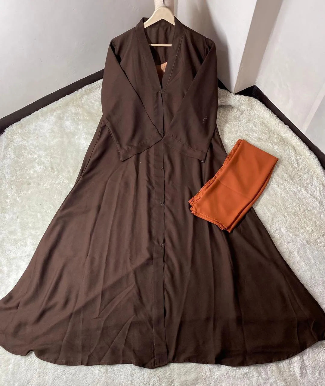 Brown dress on a hanger with an orange garment on a white surface
